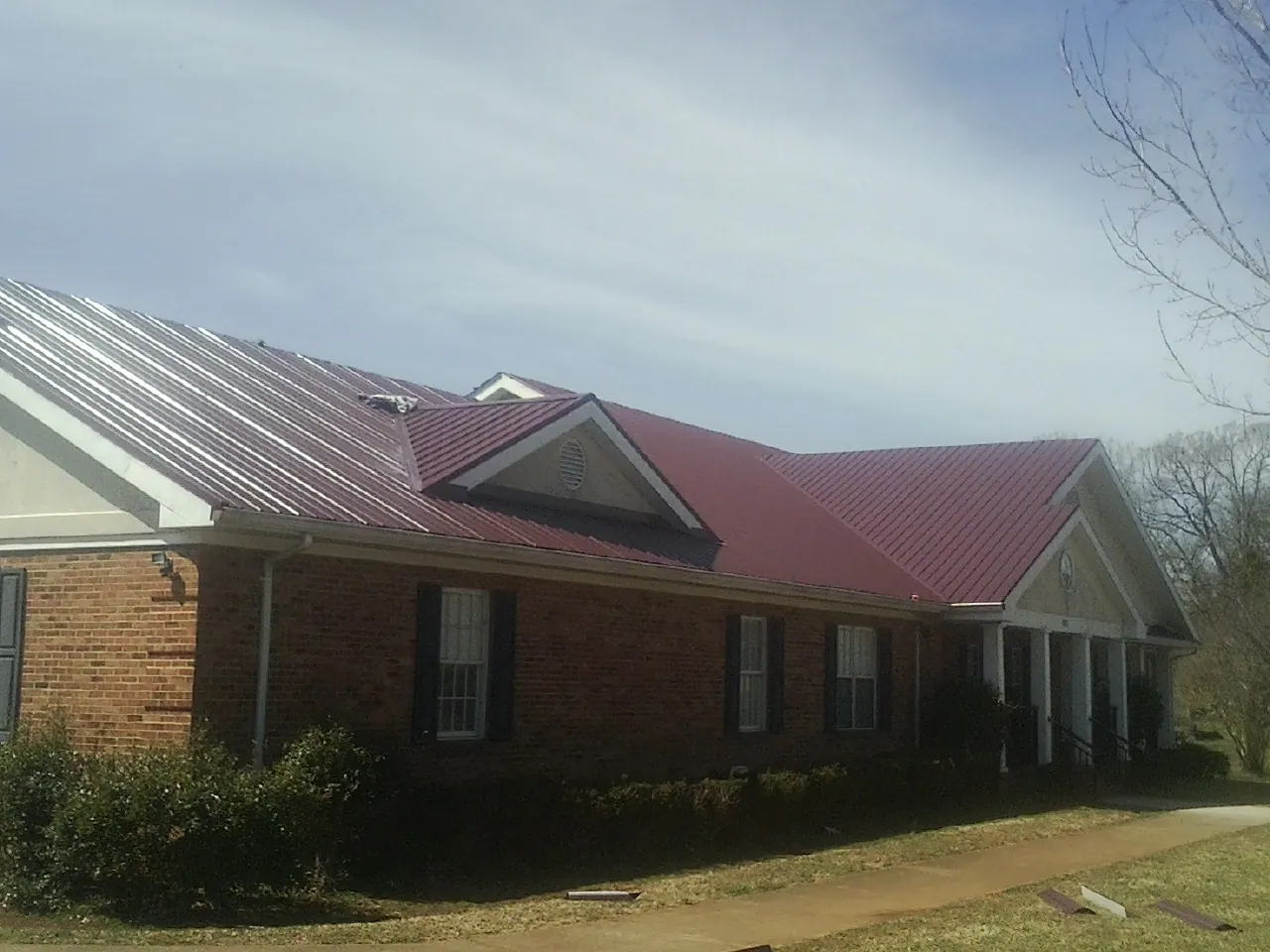Red metal roof with gabled entries on a long brick building, from a Hail Damage Roof Repair job in Aurora