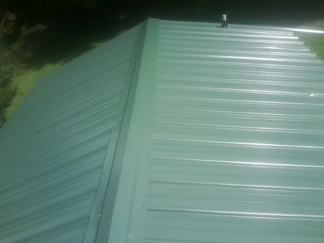 New green metal panels meeting at the ridge of a roof — Flat Roof Repair work by our crew in Aurora