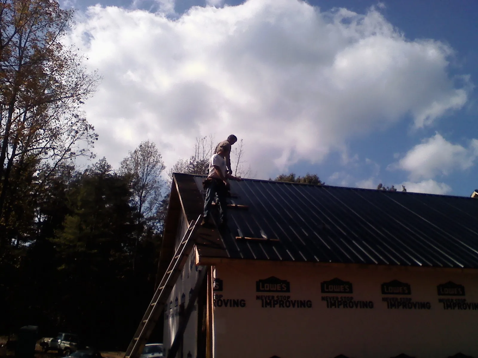 Roofer fastening dark metal panels high against a cloudy sky, from a Roof Inspection job in Aurora