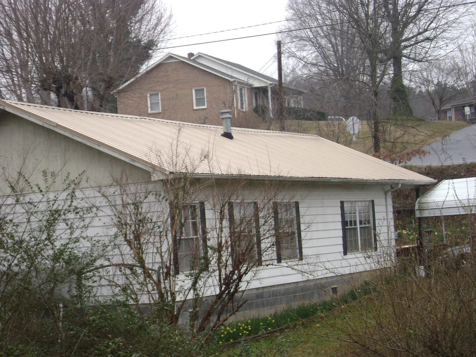 Tan metal roof on a white sided house set into a hillside — Commercial Roofing by Roofing Brothers in Aurora